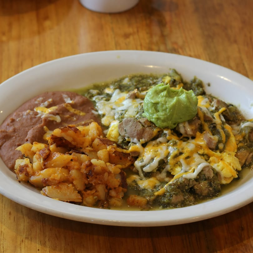 A plate of La Fogata's Mexican breakfast with green chile pork, scrambled eggs, potatoes, and refried beans.