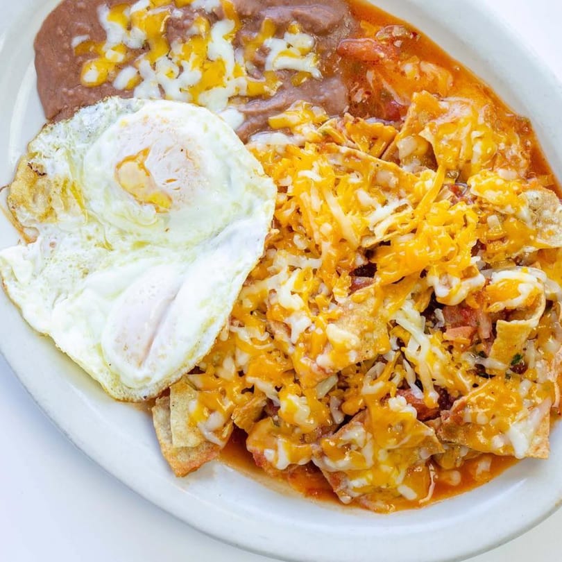 A plate of La Fogata's chilaquiles with a fried egg and refried beans, topped with melted cheese.