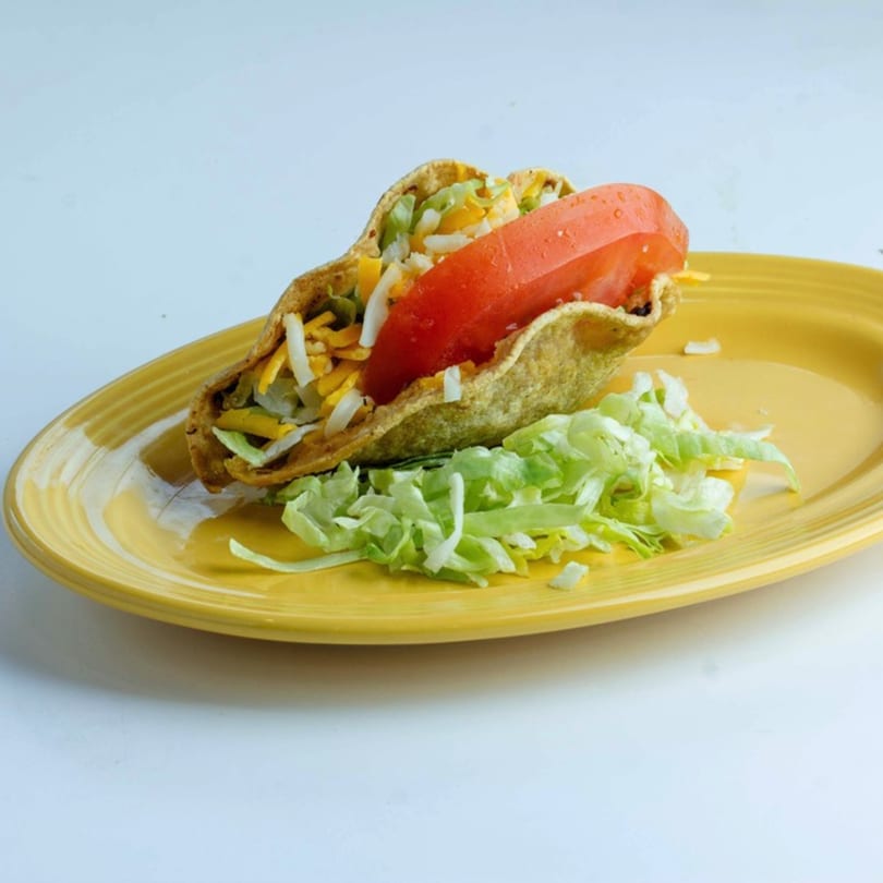 A crispy taco filled with meat, cheese, lettuce, and a large tomato slice on a yellow plate.