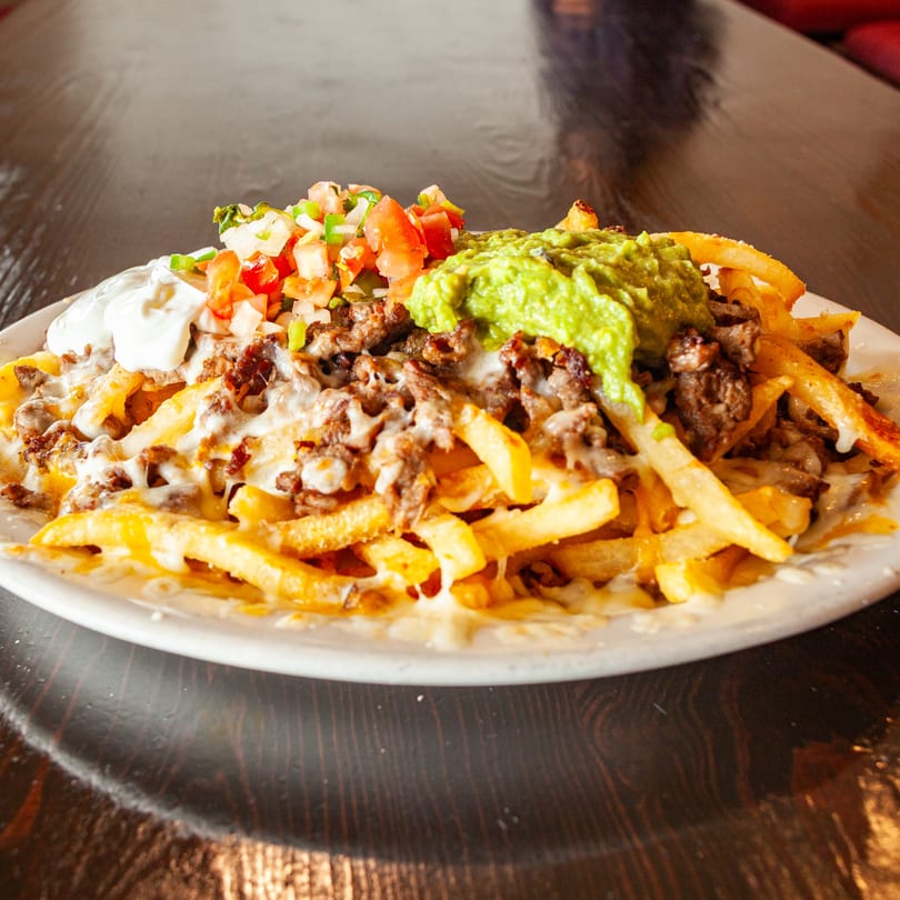 La Fogata's carne asada fries with guacamole, sour cream, and pico de gallo on a white plate.