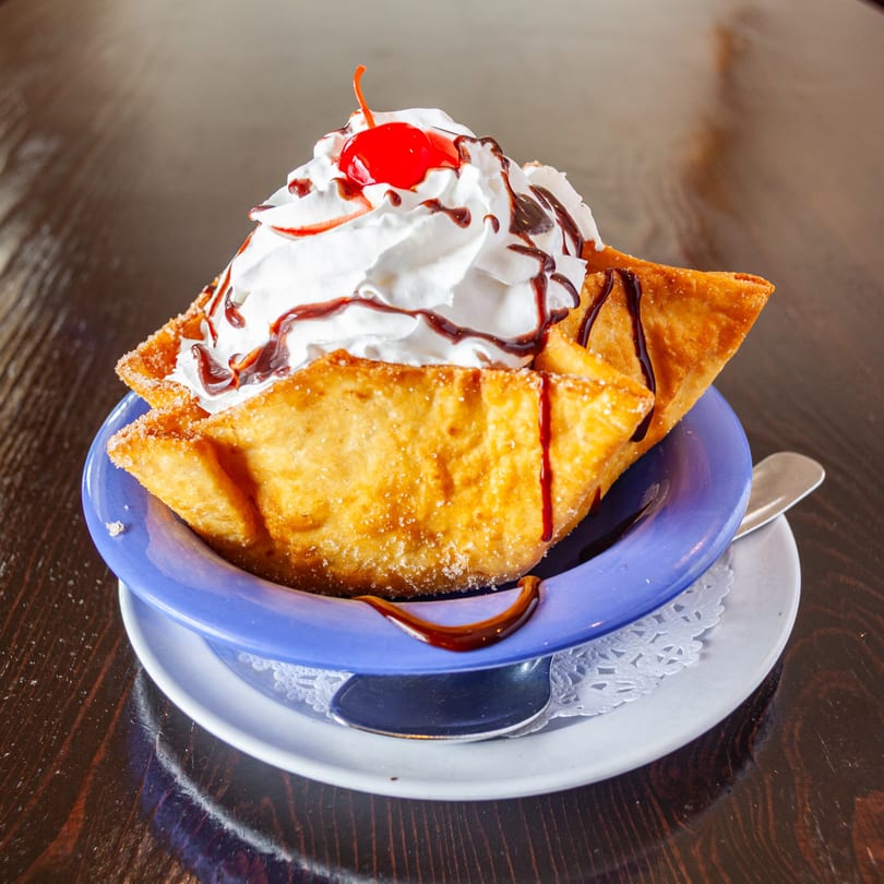 Fried ice cream dessert in a crispy shell, topped with whipped cream, chocolate syrup, and a cherry.