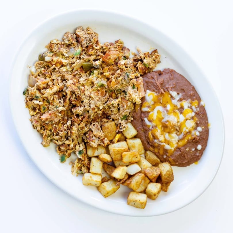 A Mexican breakfast plate with scrambled eggs, refried beans with cheese, and crispy diced potatoes.